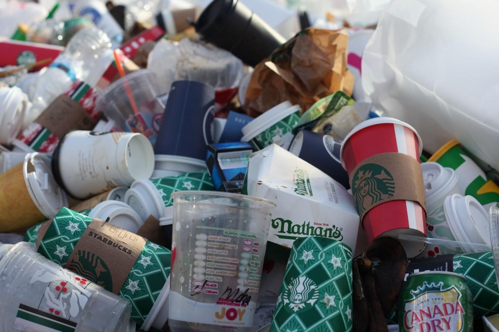 Assorted single-use packaging thrown somewhere in New York, including coffee cups, plastic cups, and some food container and plastic bottle 