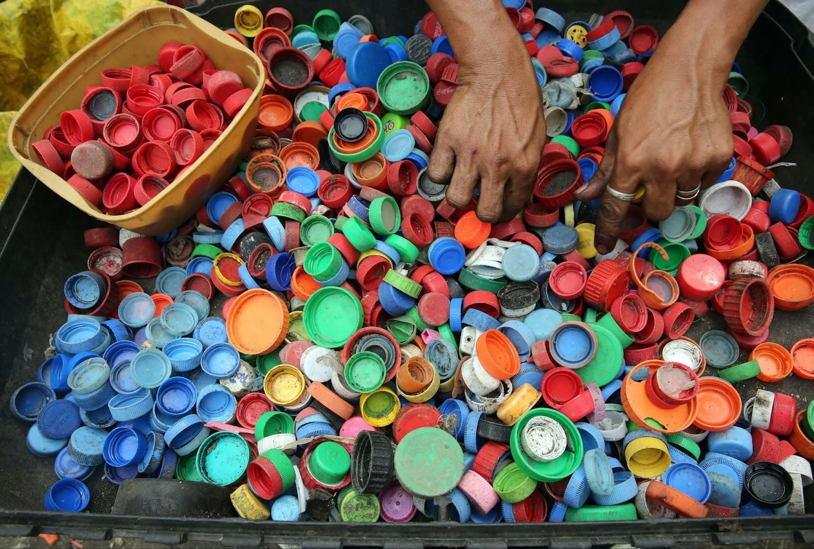 Someone manually sorting used plastic bottle caps of different colors and sizes and placing those in a separate container 