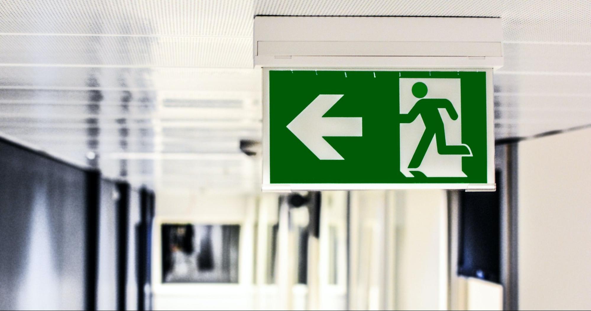 Emergency exit sign with running man icon and left direction arrow mounted on ceiling corridor