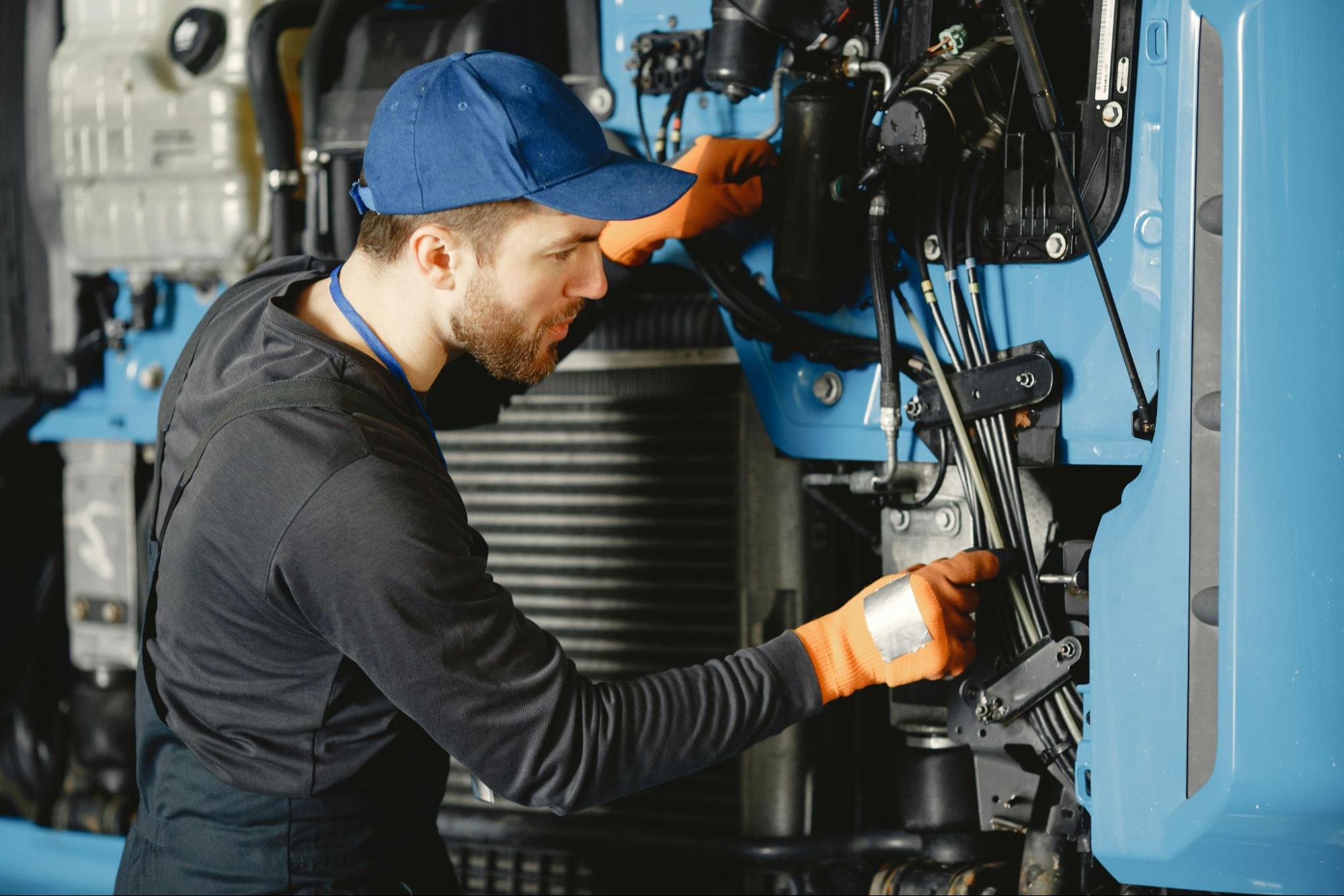 mechanic in blue cap and orange gloves working on a truck engine