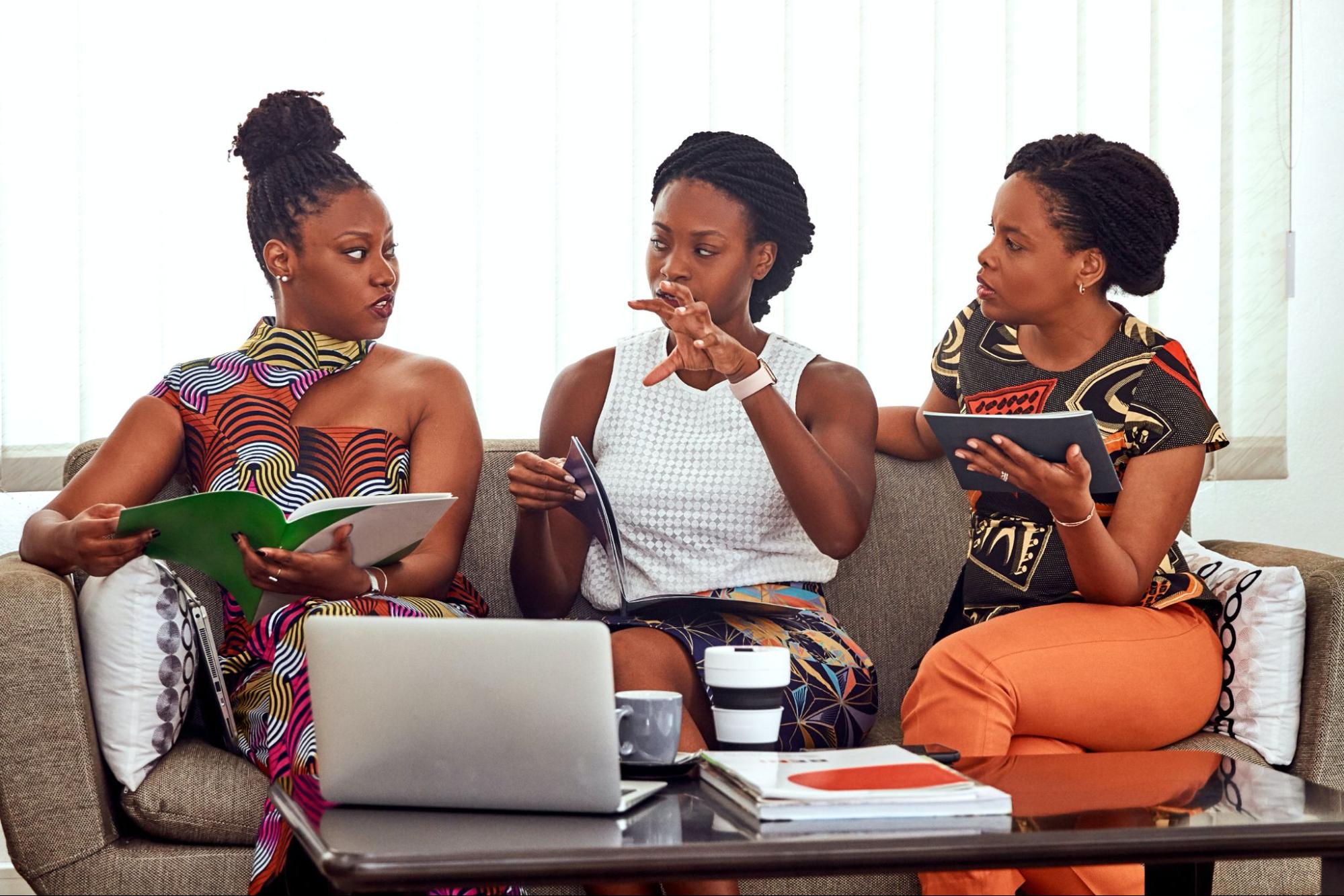 Three women on sofa discussing business brochures