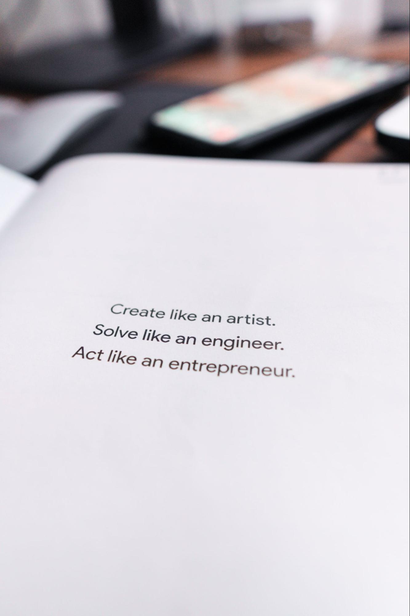 Page from book with motivational quote: “Create like an artist. Solve like an engineer. Act like an entrepreneur.