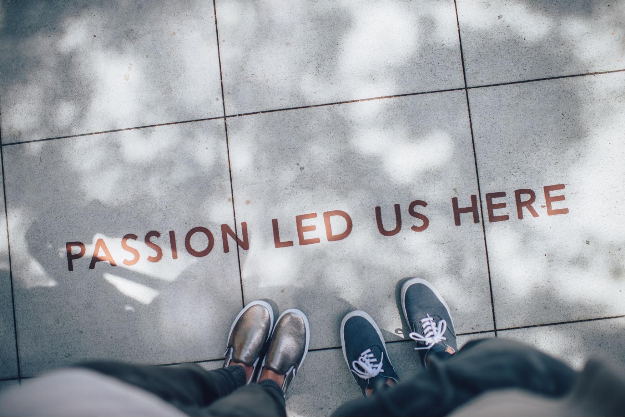 Two people standing on gray pavement, only shoes visible with text: “passion led us here”